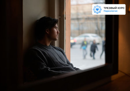 Молодой человек сидит на окне с грустным взглядом